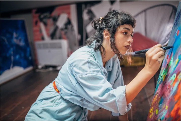 An artist drawing on a colorful canvas in her studio.